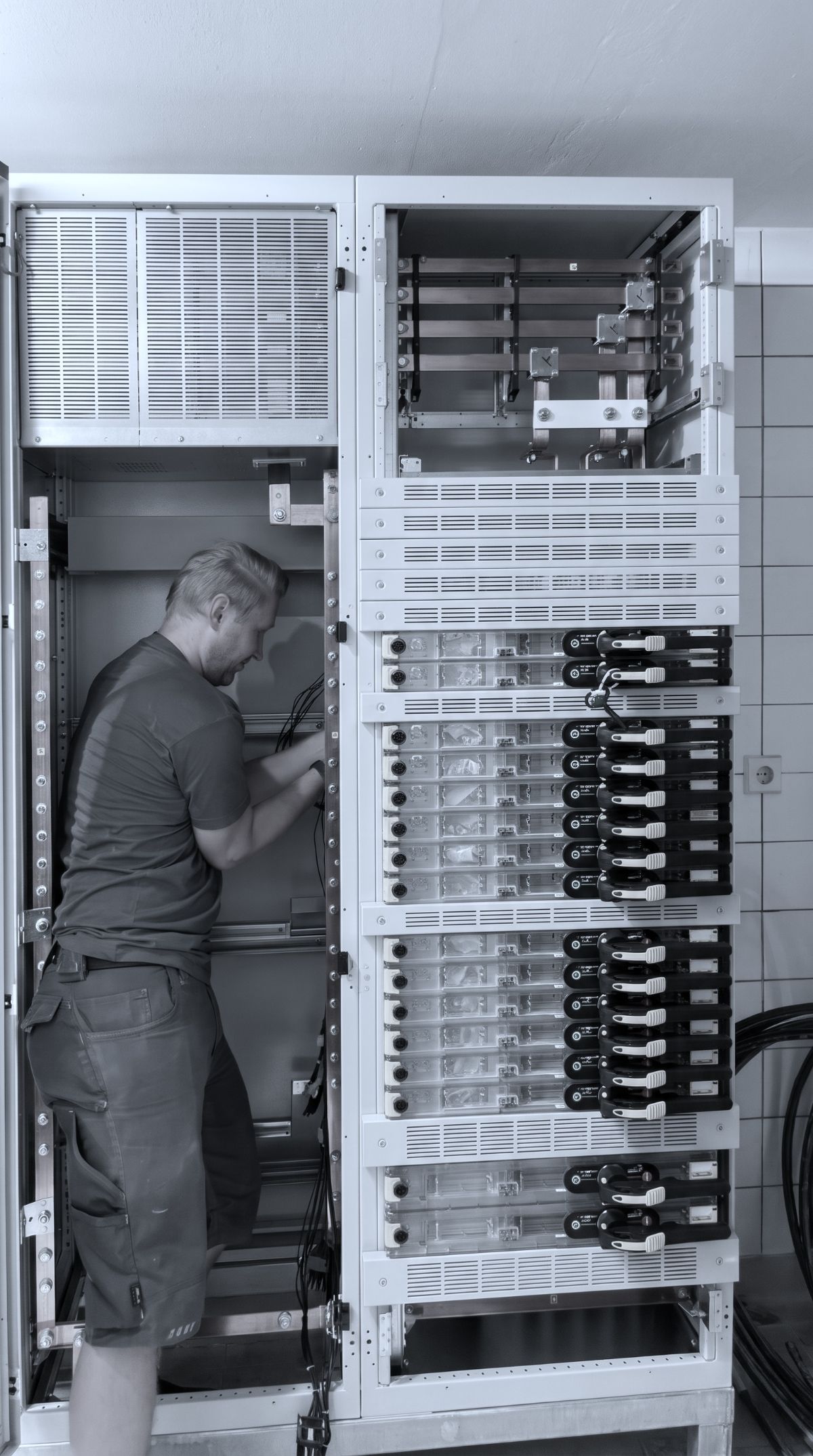 Ein Monteur arbeitet in einer großen, geöffneten Niederspannungsverteilung mit mehreren Schaltschrankfeldern.