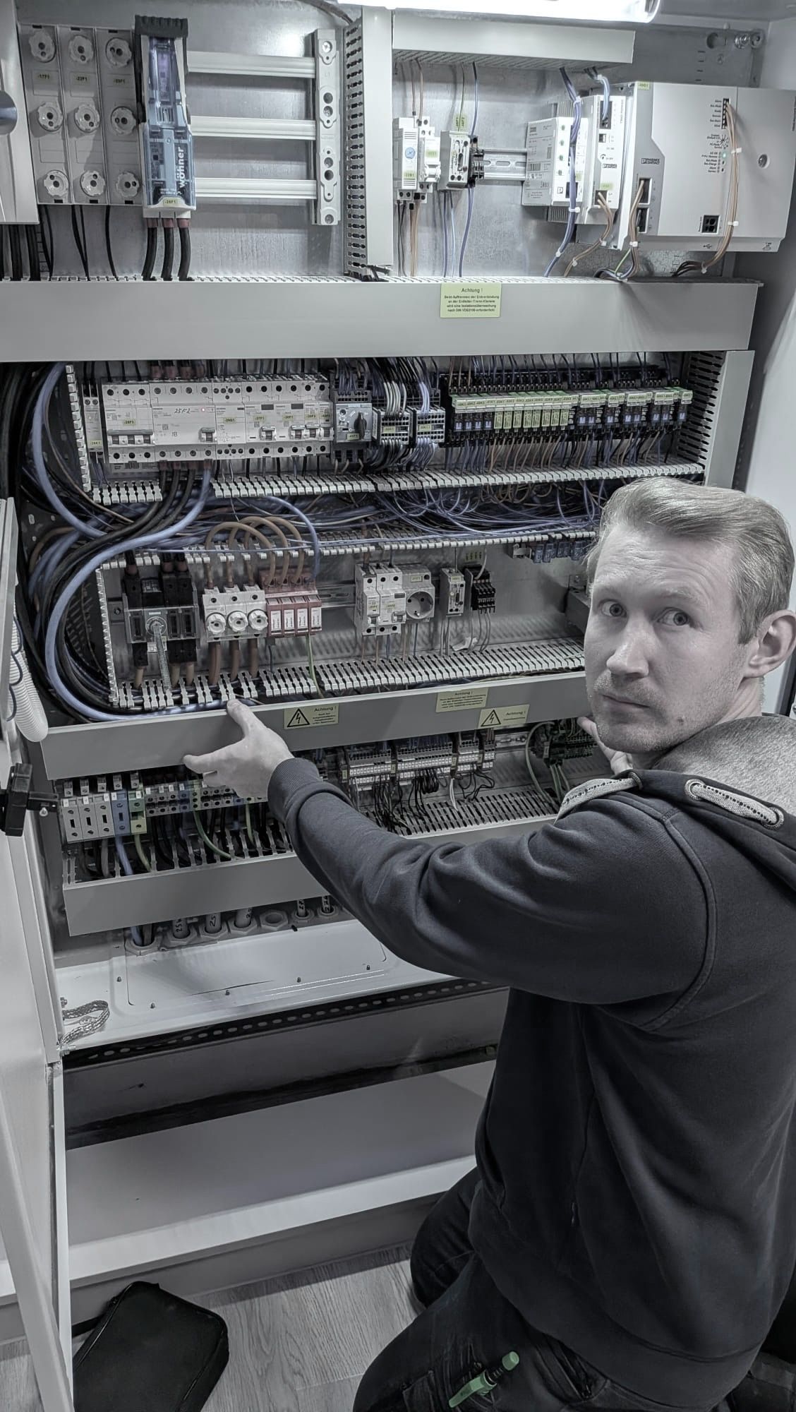 Ein Mitarbeiter von Gerhards arbeitet an einem großen, dicht verdrahteten Schaltschrank und schaut in die Kamera.